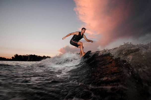 Wakesurfer silne i młody, jazda w dół rzeki fal piękne różowe niebo o zachodzie słońca - Zdjęcie, obraz
