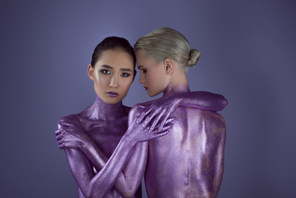 multiethnic naked girls in ultra violet glitter hugging together, isolated on purple - Photo, Image