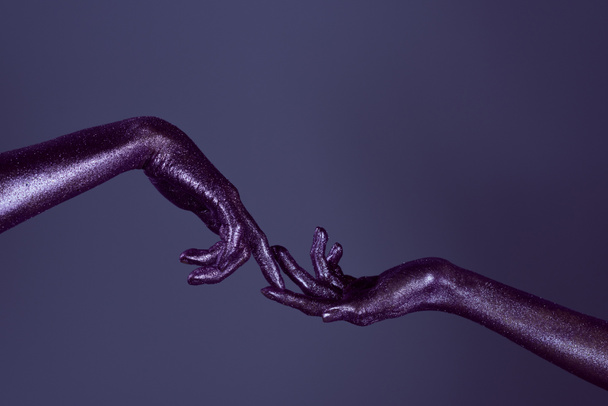 bijgesneden weergave van meisjes handen in glitter raken elkaar met vingers, geïsoleerd op paars - Foto, afbeelding