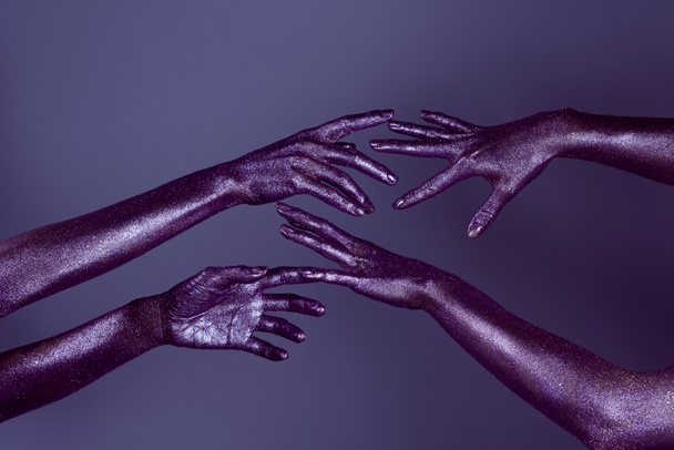 cropped view of girls hands in glitter touching each other, isolated on purple - Фото, зображення