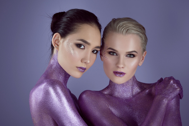 multiethnic beautiful girls in ultra violet glitter hugging together, isolated on purple - Foto, imagen