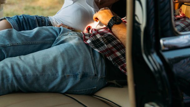black watch on man's hand.people who are lying in the car and holding hands. look through the window in the car.side view.dressed in a plaid shirt, shorts and jeans, a white blouse. doors in the car are open, seats are spread out. black car with leat - Foto, Imagen