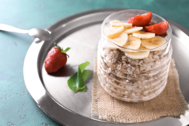 Glass jar with tasty oatmeal, sliced banana and strawberry on metal tray - Photo, Image