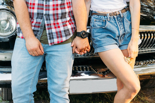 torso of a pair that is leaning on the car and holding hands in the summer. in the hands of a flower girl, on the hand of a guy wearing a black watch. date in summer.hold hands - Фото, изображение