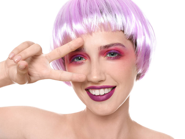 Jonge vrouw met ongebruikelijke haar en professionele make-up overwinning gebaar toont op witte achtergrond - Foto, afbeelding