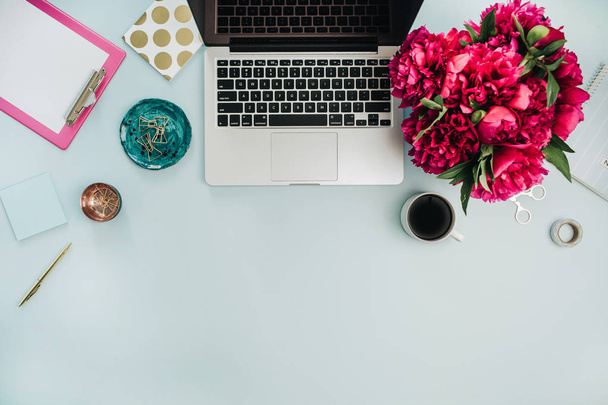 Espace de travail avec ordinateur portable et bouquet de fleurs de pivoine rose sur fond bleu. Couchage plat, vue sur le dessus bureau à domicile
. - Photo, image