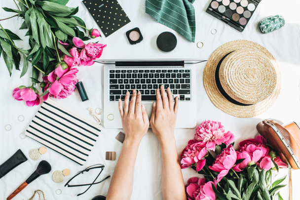 flacher Schreibtisch mit Laptop, rosa Pfingstrosenblumen, Kosmetik, Accessoires. Frau, die am Computer arbeitet. Mode oder Beauty Blog Hintergrund. - Foto, Bild