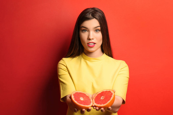 Beautiful young woman with halves of grapefruit on color background - Photo, Image