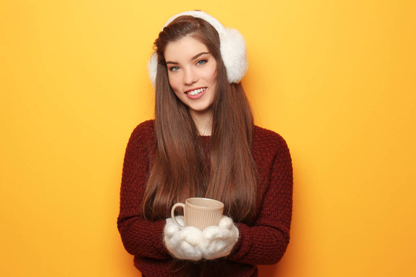 Hermosa mujer joven en ropa de abrigo sosteniendo la taza de té caliente en el fondo de color
 - Foto, imagen