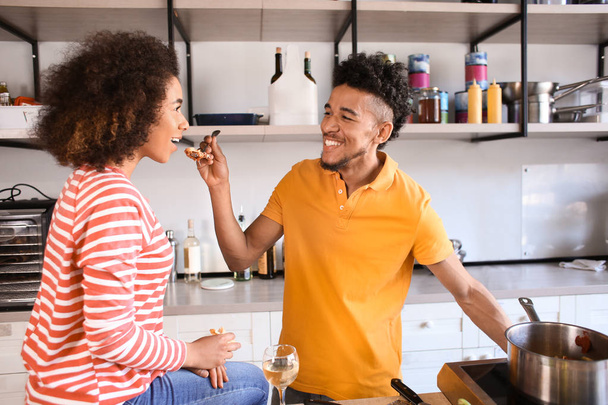 Young African-American man feeding his girlfriend in kitchen - Foto, imagen