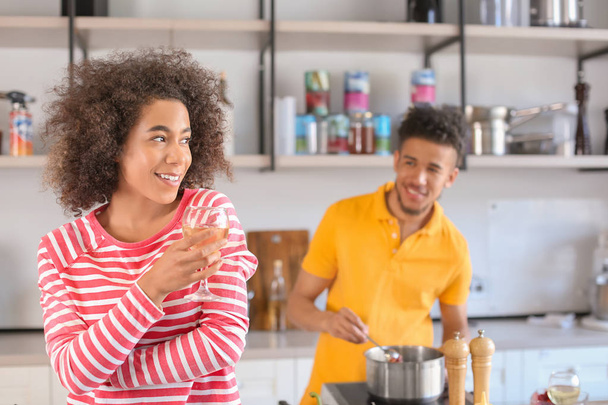 Giovane donna afroamericana che beve vino e il suo fidanzato che cucina in cucina
 - Foto, immagini