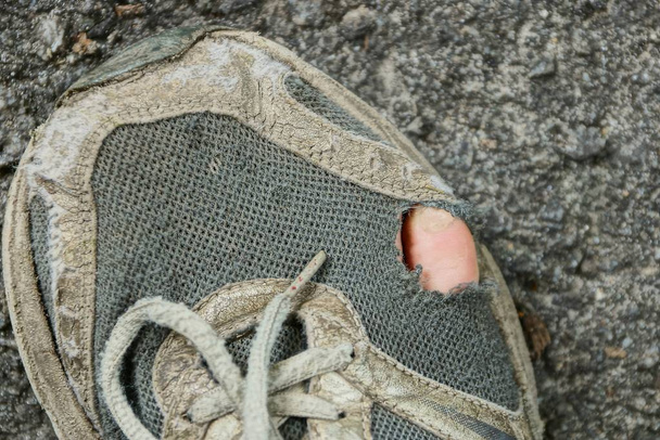 gray old ragged sneaker with a finger on the asphalt - Photo, Image