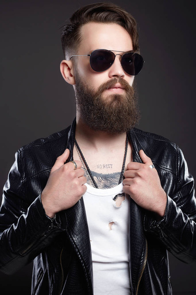 fashionable handsome man with tattoo and sunglasses. Hipster bearded Sexy boy in leather coat and trendy glasses - 写真・画像