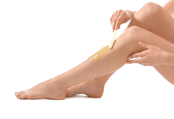 Mujer joven depilándose la pierna con azúcar líquida sobre fondo blanco
 - Foto, imagen
