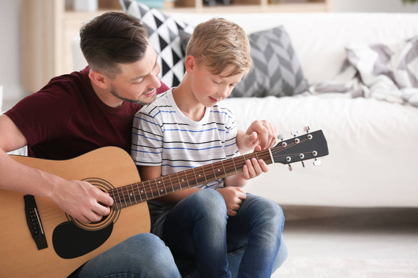 Father teaching his son to play guitar at home - Foto, imagen