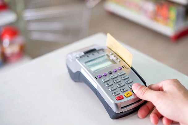 Mão imprensa com cartão de crédito deslizante no terminal de pagamento no supermercado
 - Foto, Imagem
