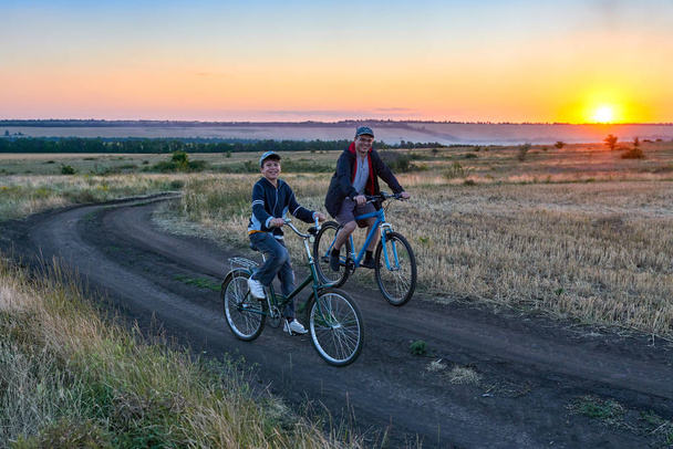 Vater und Sohn fahren abends mit dem Fahrrad auf dem Feld - Foto, Bild