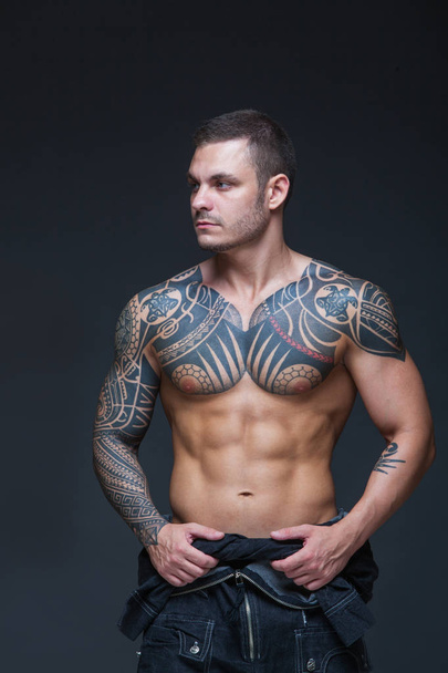 The man with a muscular naked torso with tattoos on the dark background. ABS - Foto, Imagen