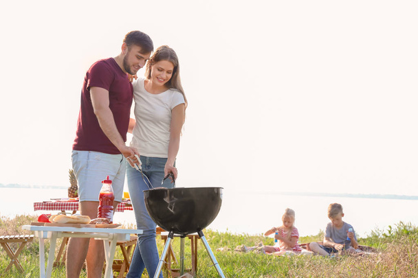 Happy young couple cooking tasty food on barbecue grill outdoors. Family picnic - Photo, Image