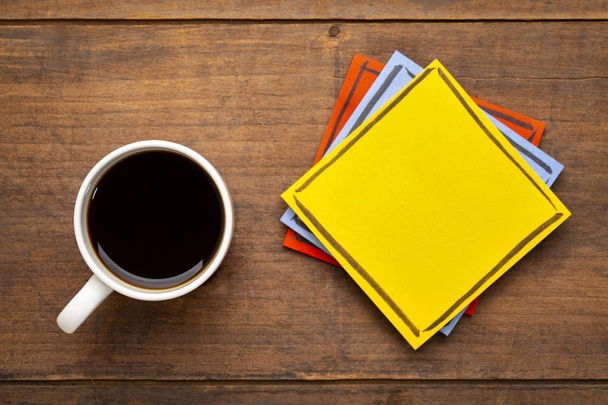 yellow, blank reminder note on a grunge wooden table with a cup of espresso coffee - Fotoğraf, Görsel