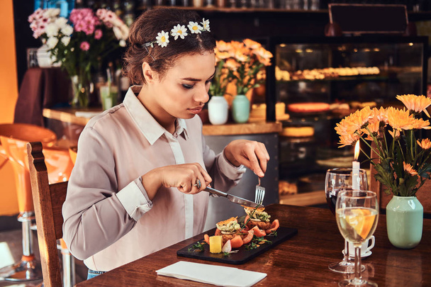 Nahaufnahme Porträt einer schönen schwarzhäutigen Frau mit Bluse und Blumenstirnband, die beim Essen in einem Restaurant das Abendessen genießt. - Foto, Bild