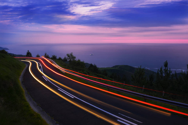 Sentiers lumineux de voiture sur la route par la mer contre le ciel, coucher de soleil, mont Jaizkibel, Pays Basque
 - Photo, image