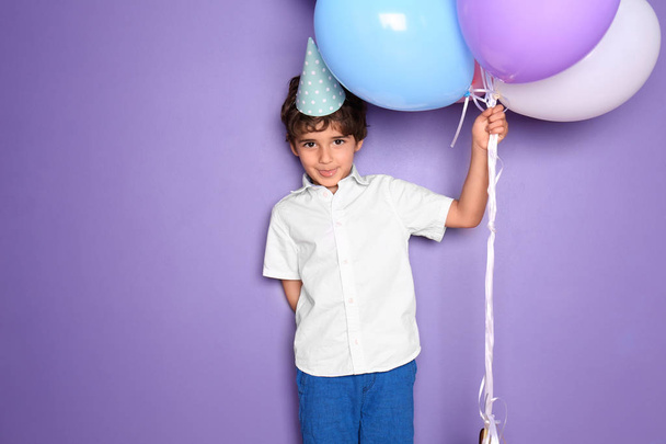 Χαριτωμένο μικρό αγόρι με μπαλόνια σε έγχρωμο φόντο. Γιορτή των γενεθλίων - Φωτογραφία, εικόνα