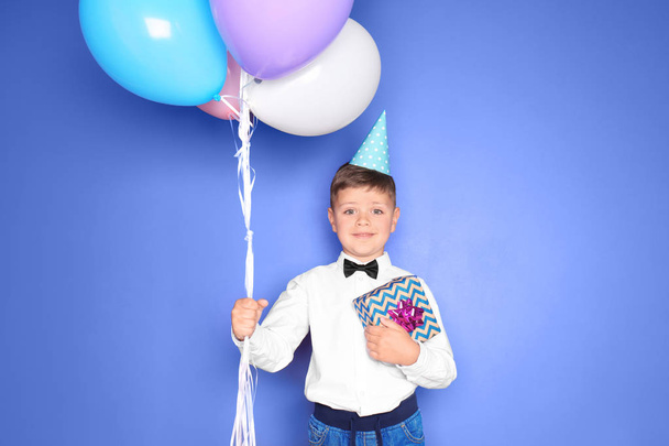 Cute little boy with balloons and gift for his birthday and on color background - Photo, Image