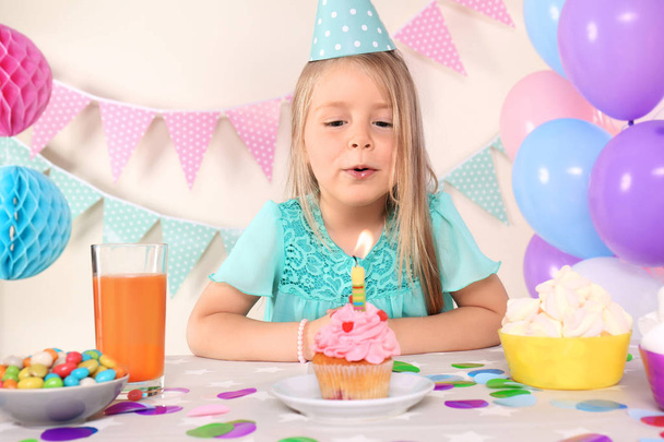 Μικρό κορίτσι φυσάει κερί σε cupcake γενέθλια στο σπίτι - Φωτογραφία, εικόνα