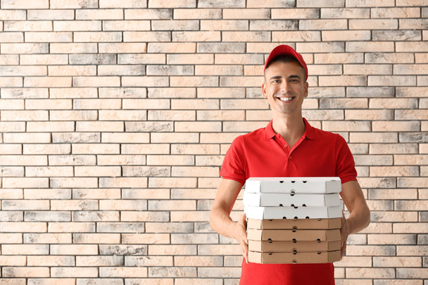 Nuori mies pizzalaatikoiden kanssa tiiliseinää vasten. Elintarvikkeiden jakelupalvelu
 - Valokuva, kuva