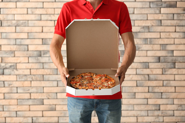 Young man holding box with tasty pizza against brick wall. Food delivery service - Photo, Image
