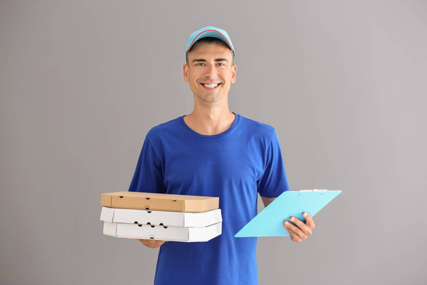 junger Mann mit Pizzakartons und Klemmbrett auf grauem Hintergrund. Essenslieferdienst - Foto, Bild