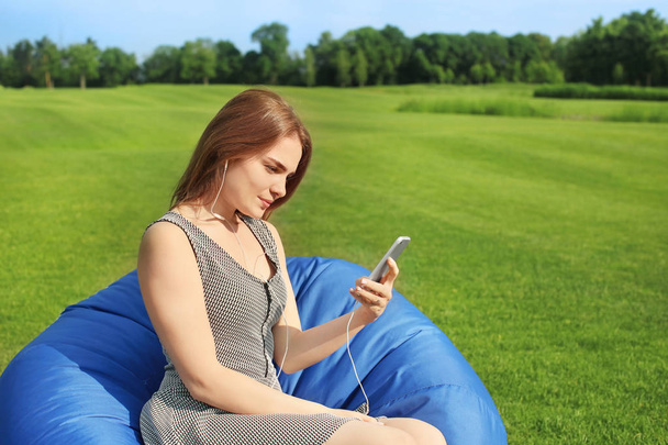 Young woman listening to music while sitting on bean bag chair outdoors - Photo, Image