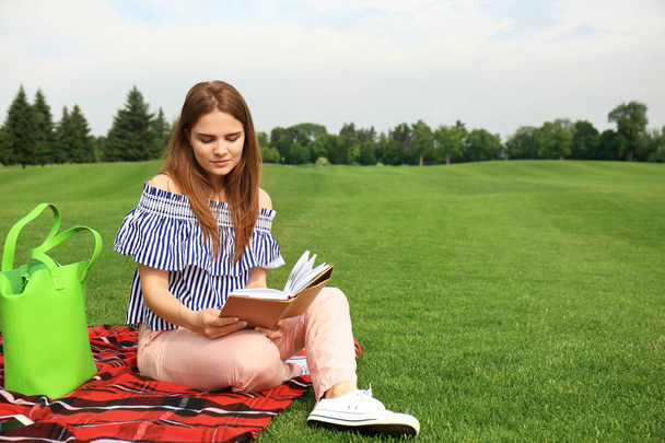 Young woman with book resting on plaid outdoors - Foto, imagen