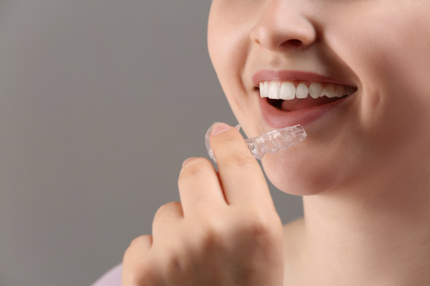 Woman putting occlusal splint in mouth on grey background, closeup - Photo, Image