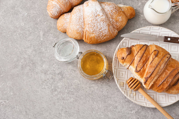 Teller mit leckerem Croissant und Honig auf grauem Hintergrund - Foto, Bild