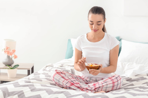 Bella giovane donna mangiare gustosa farina d'avena per la prima colazione in camera da letto
 - Foto, immagini