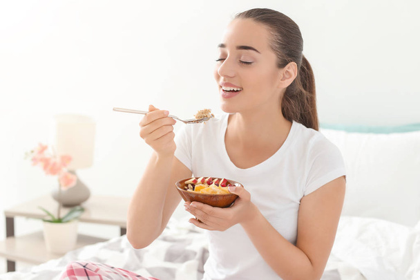 Beautiful young woman eating tasty oatmeal for breakfast in bedroom - Photo, Image