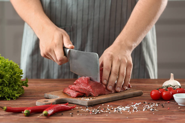 Mies leikkaa raakaa lihaa puulaudalla keittiössä
 - Valokuva, kuva