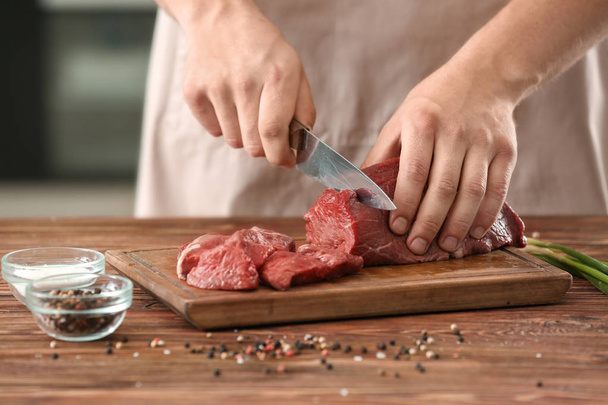 Homme coupant de la viande crue sur une planche en bois dans la cuisine
 - Photo, image