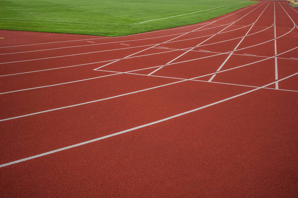 красная беговая дорожка текстура с белой маркировкой полосы возле зеленого травяного футбольного поля на стадионе спортивного пространства
 - Фото, изображение