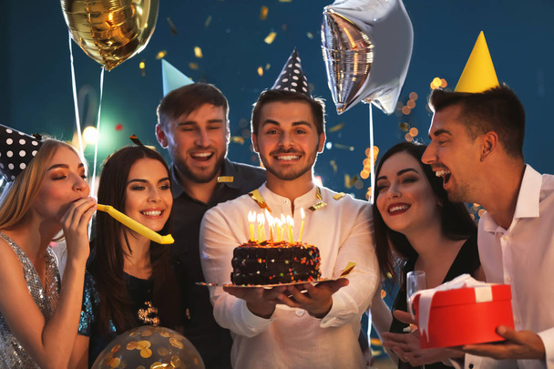 Young man with tasty cake and his friends at birthday party in club - Photo, image