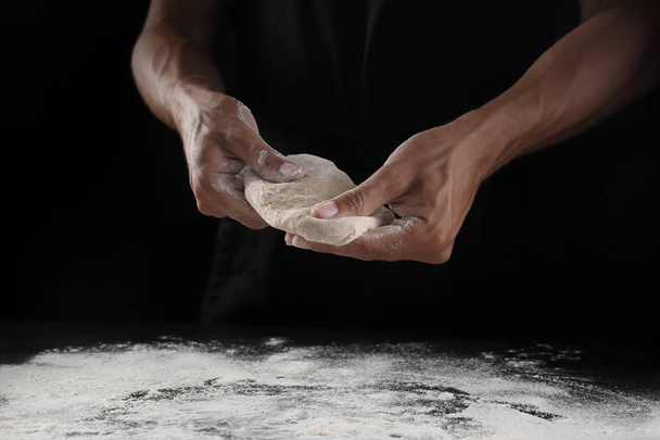 Man kneading dough on black background - Фото, изображение