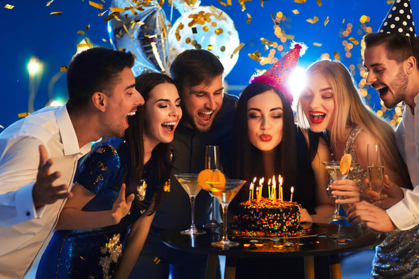 Mujer joven soplando velas en su pastel de cumpleaños con amigos en el club
 - Foto, Imagen