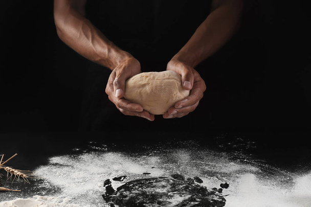 Man holding raw dough on black background - Photo, Image