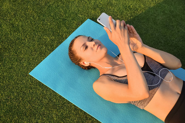 Bella giovane donna che ascolta musica mentre si trova sul tappeto yoga all'aperto
 - Foto, immagini