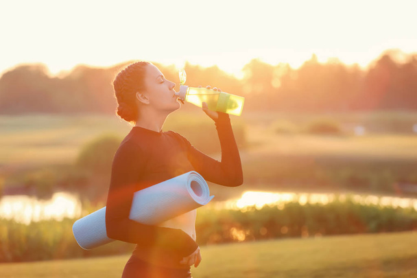 Kaunis nuori nainen juo vettä joogaharjoitusten jälkeen ulkona aamulla
 - Valokuva, kuva
