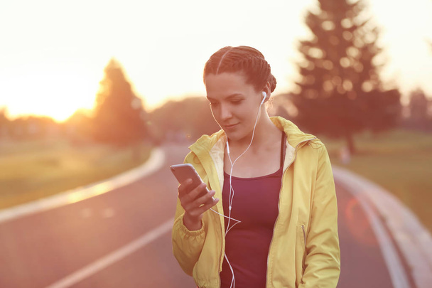 Mujer joven y deportiva con teléfono móvil escuchando música al aire libre en la mañana
 - Foto, imagen