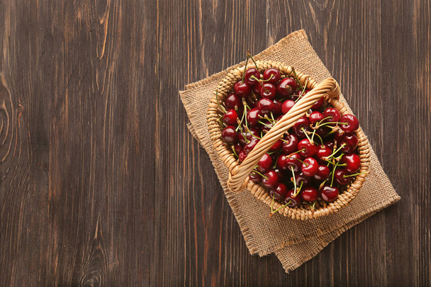 Cesta de vime com cerejas saborosas na mesa de madeira
 - Foto, Imagem