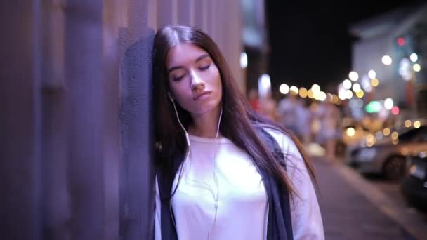 Frau hört Musik und lehnt sich entspannt an Wand in nächtlicher Stadt - Filmmaterial, Video